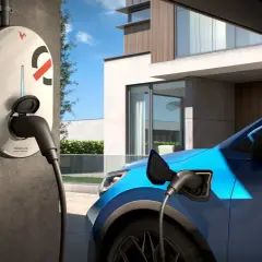 Borne de recharge électrique connectée à une voiture bleue devant une maison moderne. Idéal pour savoir où recharger voiture électrique.