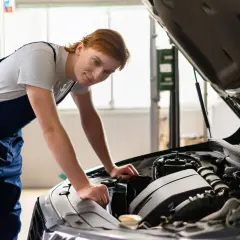 Mécanicien souriant vérifiant le moteur d'une Seat Ibiza ouverte. Il porte une combinaison bleue.