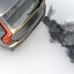 Vue aérienne d'un SUV gris émettant une épaisse fumée noire d'échappement, symbolisant la pollution.
