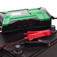 Chargeur de batterie vert et noir connecté à une batterie de voiture. Idéal pour le maintien de charge batterie sans débrancher.