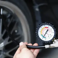 Main tenant vérifie la pression du pneu de voiture avec un manomètre. Il est prêt à gonfler le pneu.