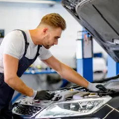 Mécanicien concentré sur le moteur d'une voiture, cherchant une astuce pour essuie glace en panne.