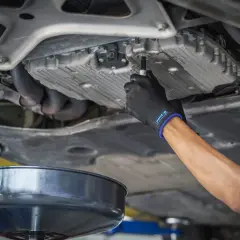 Main d'un mécanicien en gant noir dévissant le bouchon de vidange d'une voiture diesel. Le prix de la vidange voiture diesel est une préoccupation pour de nombreux propriétaires.