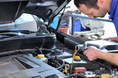 Mécanicien versant de l'huile moteur dans une Clio 2. Le prix de la vidange est abordable pour maintenir votre véhicule en bon état.
