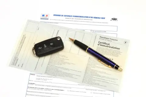 Carte grise, clé de voiture et stylo sur un document officiel.