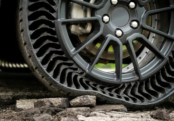 Gros plan sur une roue de voiture avec un pneu increvable, composé de multiples alvéoles noires, posé sur un sol dégradé.
