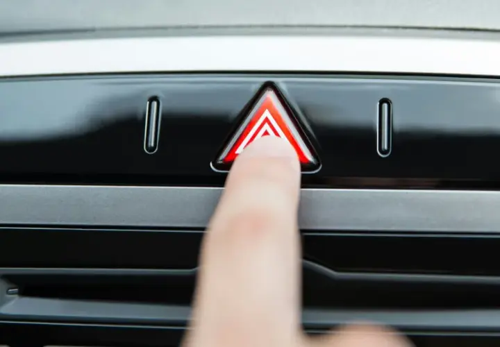 Un doigt appuie sur le bouton des feux de détresse, un triangle rouge lumineux sur le tableau de bord d'une voiture.