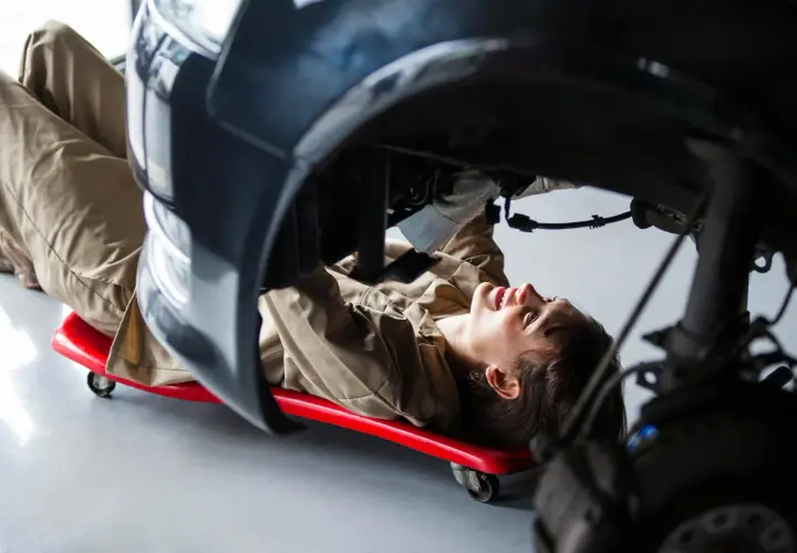 Mécanicienne travaillant sous une voiture, utilisant un chariot pour accéder à une pièce de réemploi.