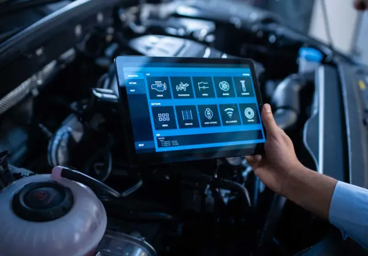 Un technicien utilise une tablette pour un suivi entretien voiture gratuit, diagnostiquant le moteur et les systèmes.