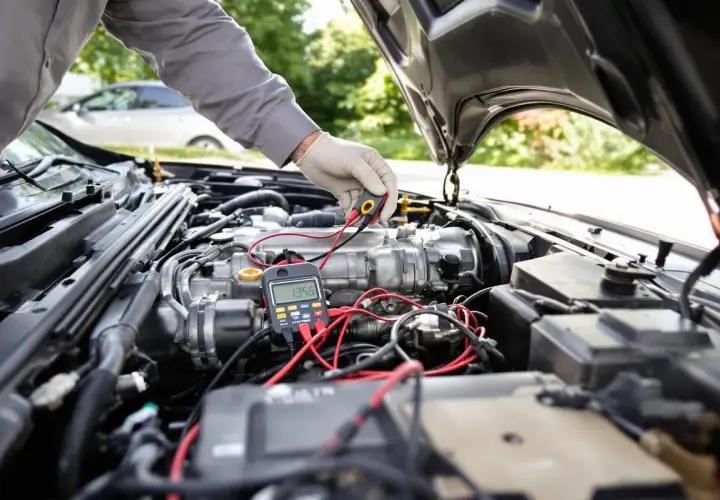 Mécanicien vérifiant le moteur d'une voiture avec un multimètre, diagnostiquant un possible problème démarreur voiture.