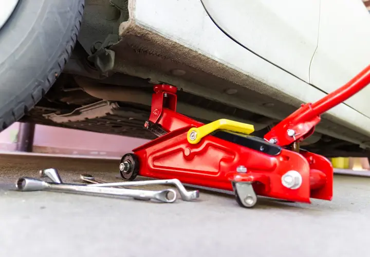 Un cric rouge est utilisé pour soulever une voiture. Des clés sont posées au sol, prêtes à être utilisées pour changer une roue.