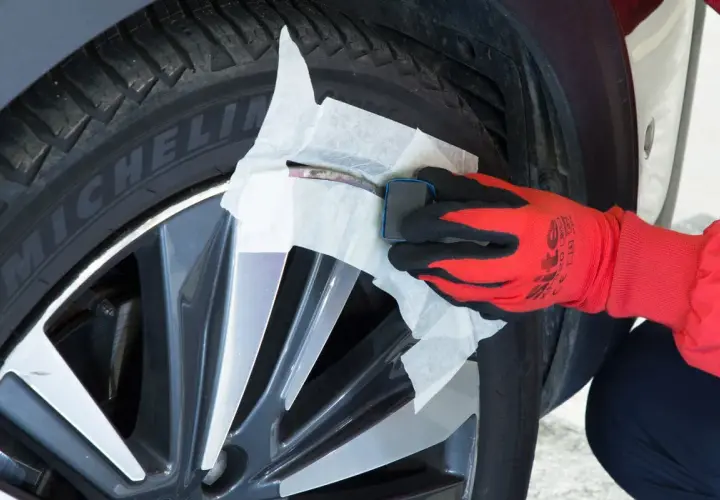 Main d'une personne portant un gant rouge et noir, utilisant un produit pour réparer jante alu.