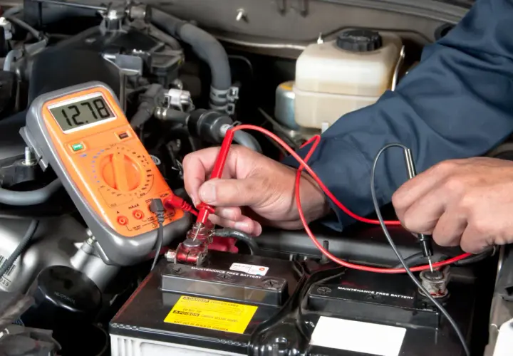 Un mécanicien vérifie la tension de la batterie d'une Mini Cooper. L'emplacement de la batterie est sous le capot, accessible pour le diagnostic.