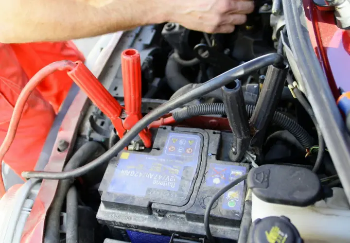 Comment brancher un booster de batterie : les pinces rouges et noires sont connectées à la batterie d'une voiture.