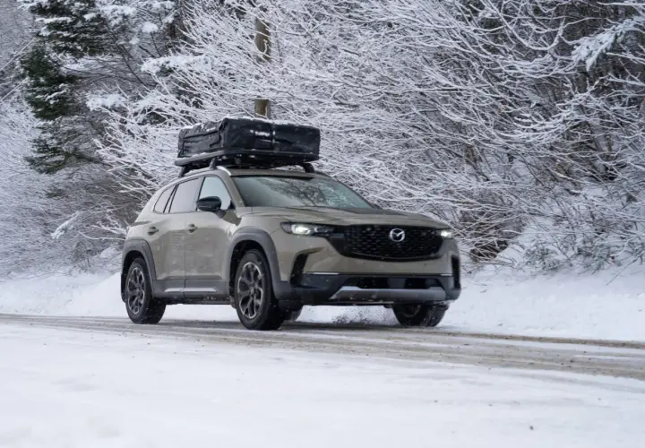 Un SUV gris roule sur une route enneigée, prêt à affronter l'hiver avec un coffre de toit chargé.