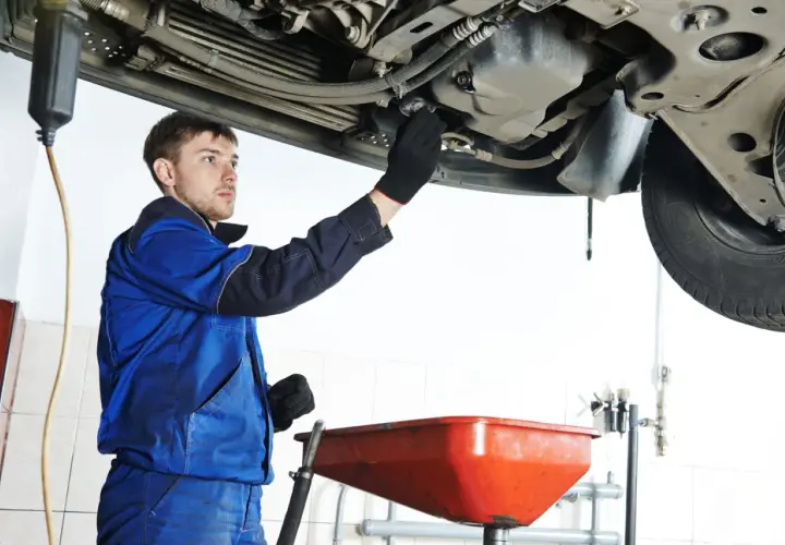 Mécanicien en bleu effectuant la vidange d'une voiture, prêt à changer l'huile. Savoir quand faire vidange voiture est essentiel.