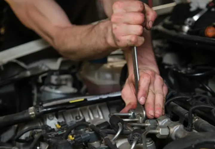 Mécanicien utilisant un outil pour tenter de comment enlever un injecteur grippé sans extracteur. Gros plan sur les mains et le moteur.