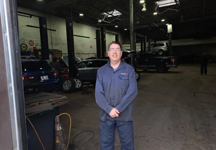 Homme souriant dans un garage libre service pour réparer soi-même. Plusieurs voitures sur des ponts élévateurs.