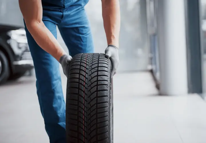Un mécanicien en bleu tient un pneu d'hiver, une sous-marque Michelin, prêt pour le montage.