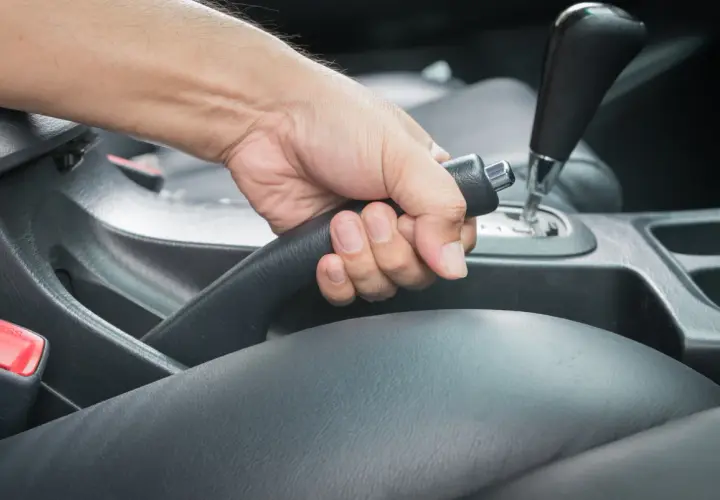 Main d'un conducteur actionnant le frein à main bloqué dans une voiture.