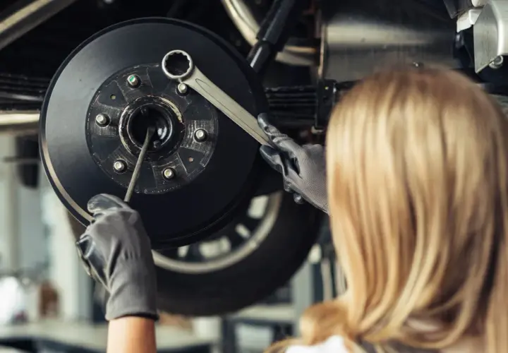 Mécanicienne travaillant sur un frein, vérifiant un piston frein bloqué avec une clé.