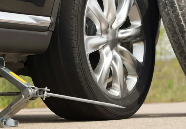 Cric de voiture soulevant un véhicule, avec une roue de secours à proximité.