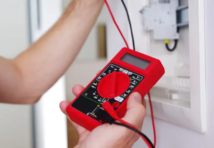 Main rouge pour tester un fusible voiture avec un multimètre.