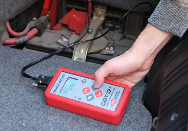 Utilisation d'un testeur de batterie avancé pour savoir comment tester une batterie sans multimètre. L'appareil affiche 12.14V.