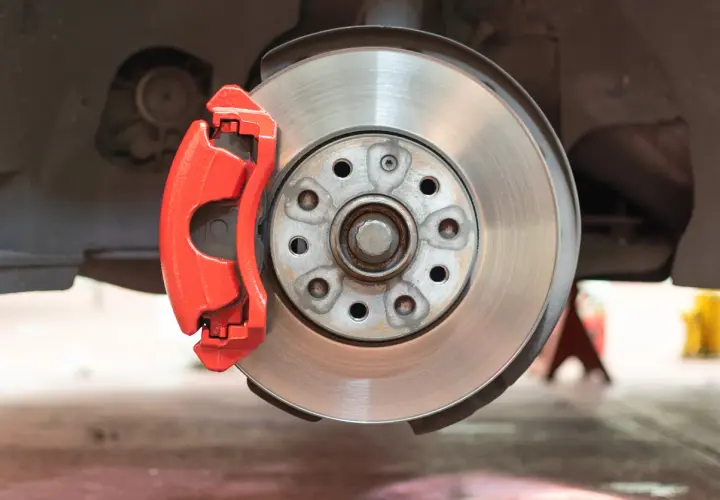 Gros plan sur un disque de frein usé, avec un étrier rouge vif.
