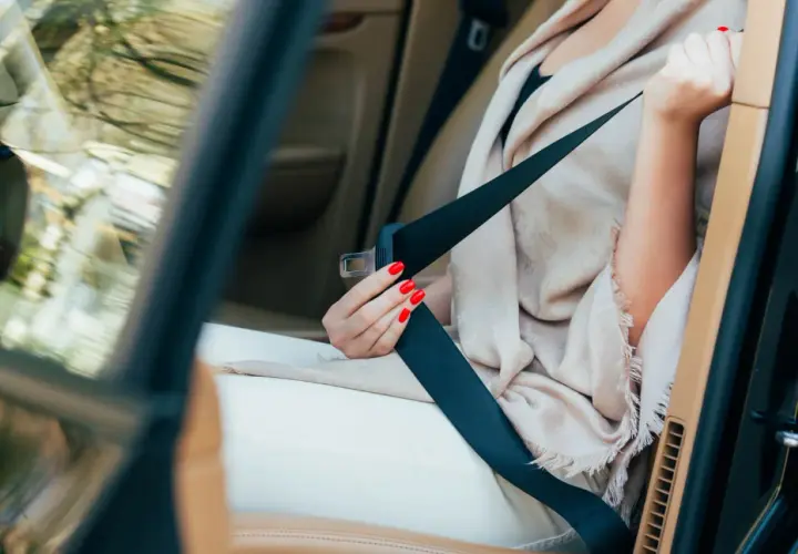 Main tenant, une femme aux ongles rouges s'apprête à changer ceinture de sécurité dans une voiture de luxe.