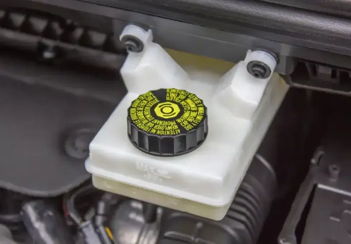 Réservoir de liquide de frein avec bouchon noir et jaune. Le niveau du liquide est visible, indiquant la nécessité d'un contrôle du liquide de frein.