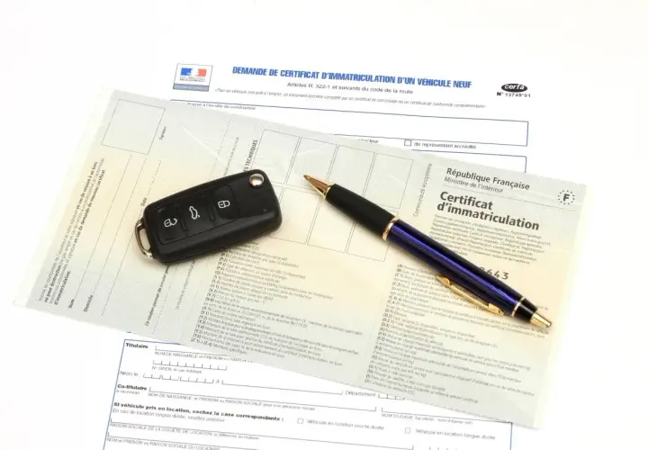 Carte grise, clé de voiture et stylo sur un document officiel.