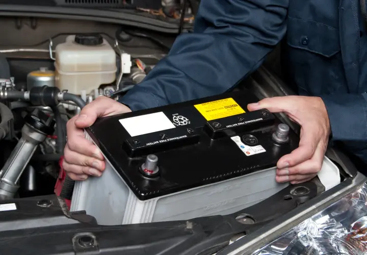 Un mécanicien installe une nouvelle batterie de voiture. Le poids de la batterie est géré avec soin.