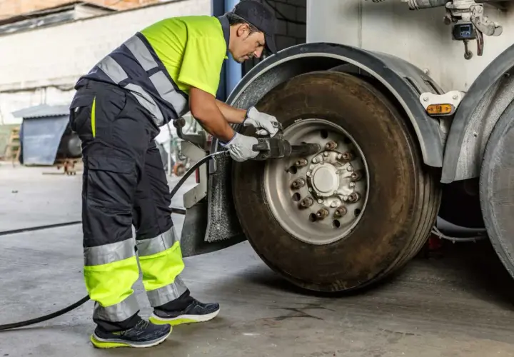 Un mécanicien en tenue de travail effectue le couple serrage roue voiture d'un camion avec une clé à chocs.