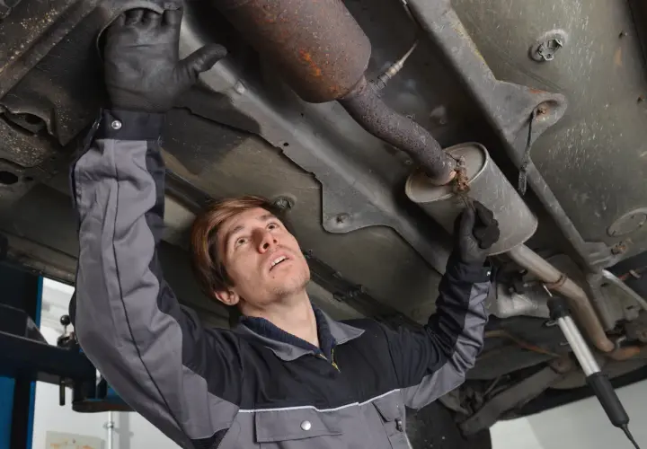 Mécanicien inspectant le pot catalytique d'une voiture, sous le véhicule.