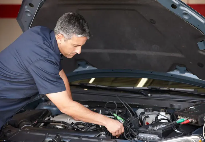 Mécanicien diagnostiquant un problème de démarrage à chaud sur un moteur de voiture avec un appareil électronique.