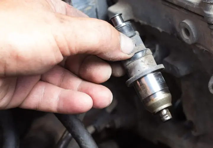 Main d'un mécanicien tenant un injecteur diesel sale, prêt à nettoyer injecteur diesel soi-même.