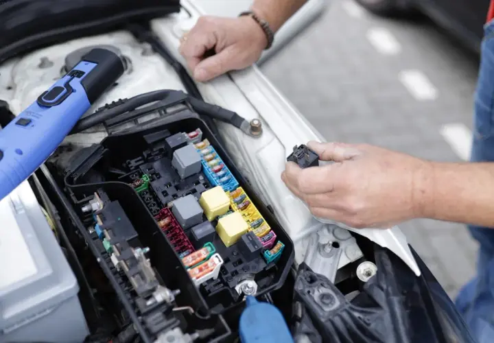 Un mécanicien examine le boîtier de fusibles d'une voiture, cherchant la cause d'un problème électrique. Il tient un relais dans sa main.