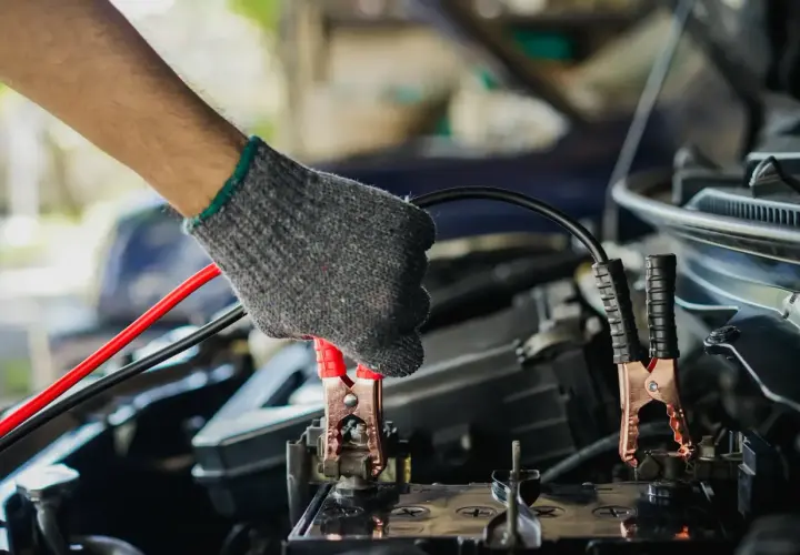 Main tenant un câble pour démarrer une voiture. La pince rouge est connectée à la batterie.