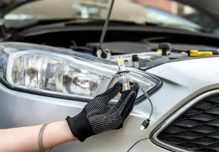 Main tenant une ampoule LED neuve, prêt à changer les ampoules de phare d'une voiture argentée.