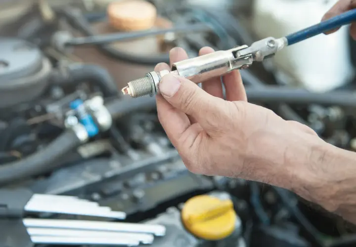 Main d'un mécanicien tenant une bougie d'allumage, prête à être installée dans le moteur d'une voiture.