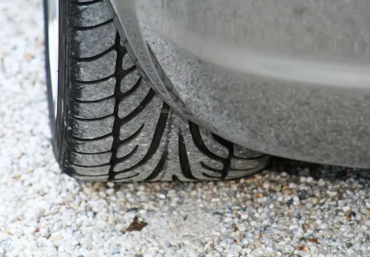 Gros plan sur un pneu de voiture usé, posé sur des graviers. J'espère que mes pneus font du bruit quand je roule, car ils sont en fin de vie !