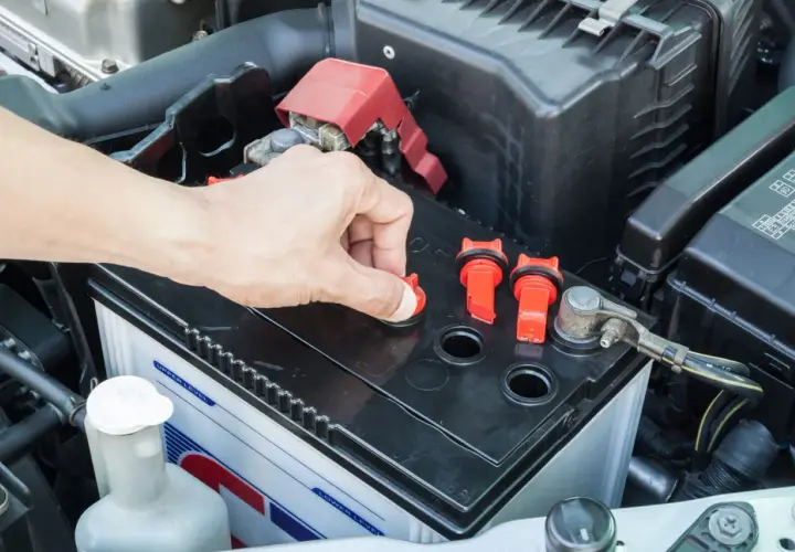 Main d'une personne ouvrant un bouchon sur une batterie de voiture, peut-être pour vérifier le niveau d'eau pour batterie.