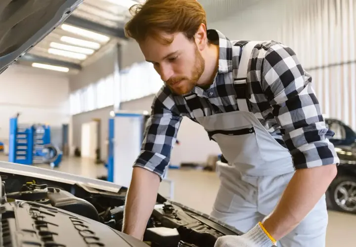 Mécanicien concentré sur le moteur d'une voiture, prêt à effectuer une vidange. Il se demande combien de litre d'huile pour une vidange.
