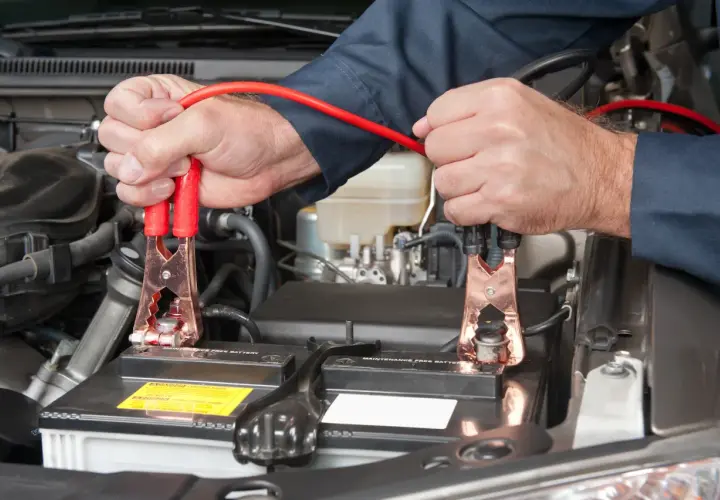 Mains de mécanicien connectant des câbles de démarrage à une batterie de voiture. On peut charger une batterie sans la débrancher.