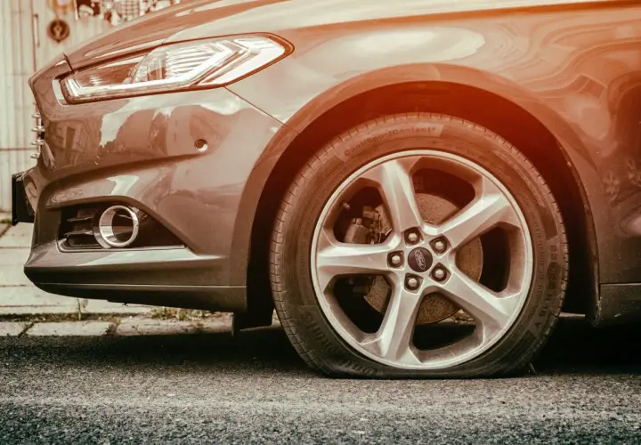 Gros plan sur une roue de voiture Ford avec un pneu crevé, le flanc complètement à plat sur l'asphalte. Une vraie galère !