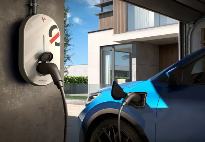 Borne de recharge électrique connectée à une voiture bleue devant une maison moderne. Idéal pour savoir où recharger voiture électrique.