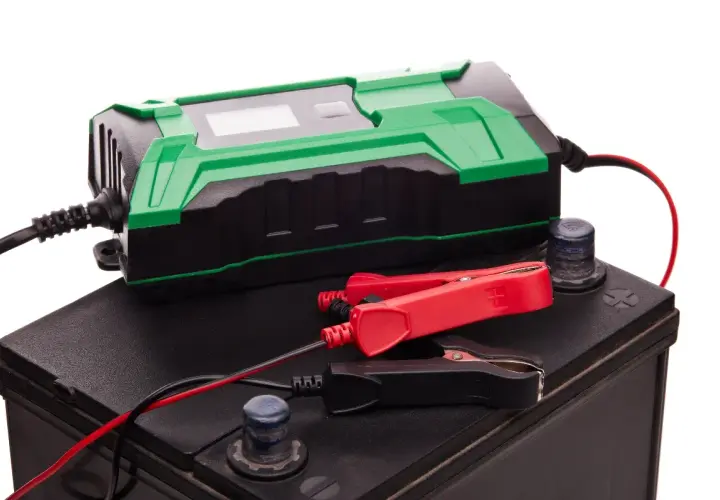 Chargeur de batterie vert et noir connecté à une batterie de voiture. Idéal pour le maintien de charge batterie sans débrancher.