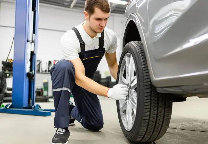 Mécanicien en salopette bleue ajustant la roue d'une voiture grise dans un garage.