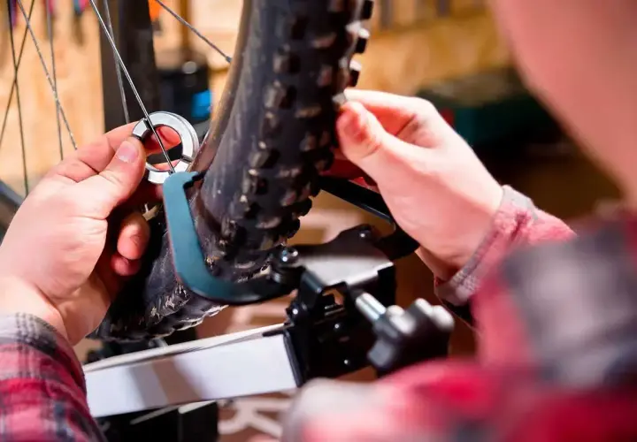 Mains ajustant un outil sur la roue voilée d'un vélo, prêt pour la réparation.